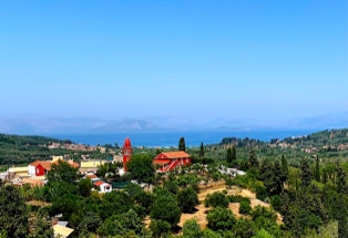 Blick vom Inselinneren über Olivenhaine mit roten Häuschen und Kirche, Korfu
